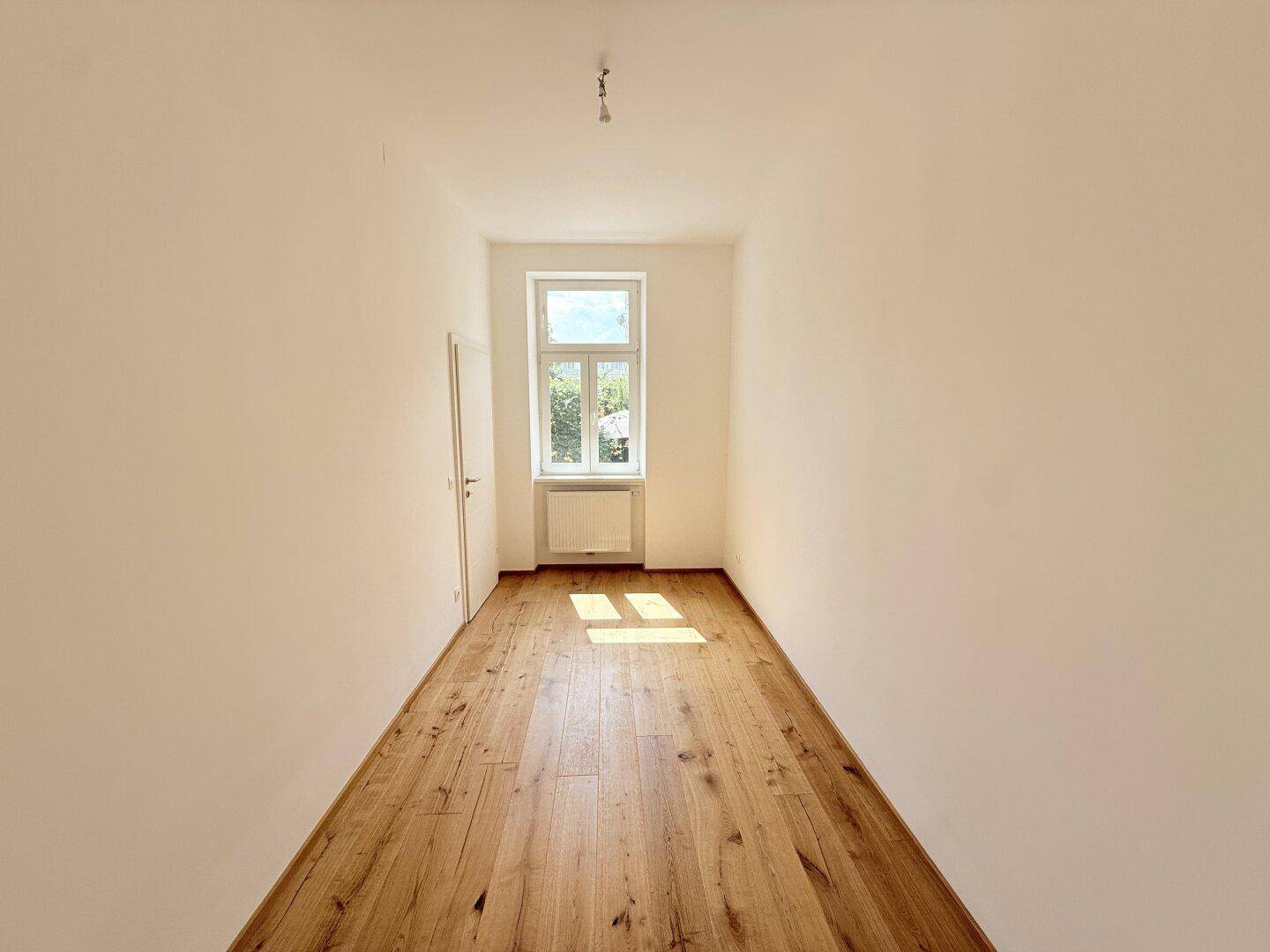 Heller, leerer Raum mit Holzboden und einem Fenster, bietet flexible Nutzung.