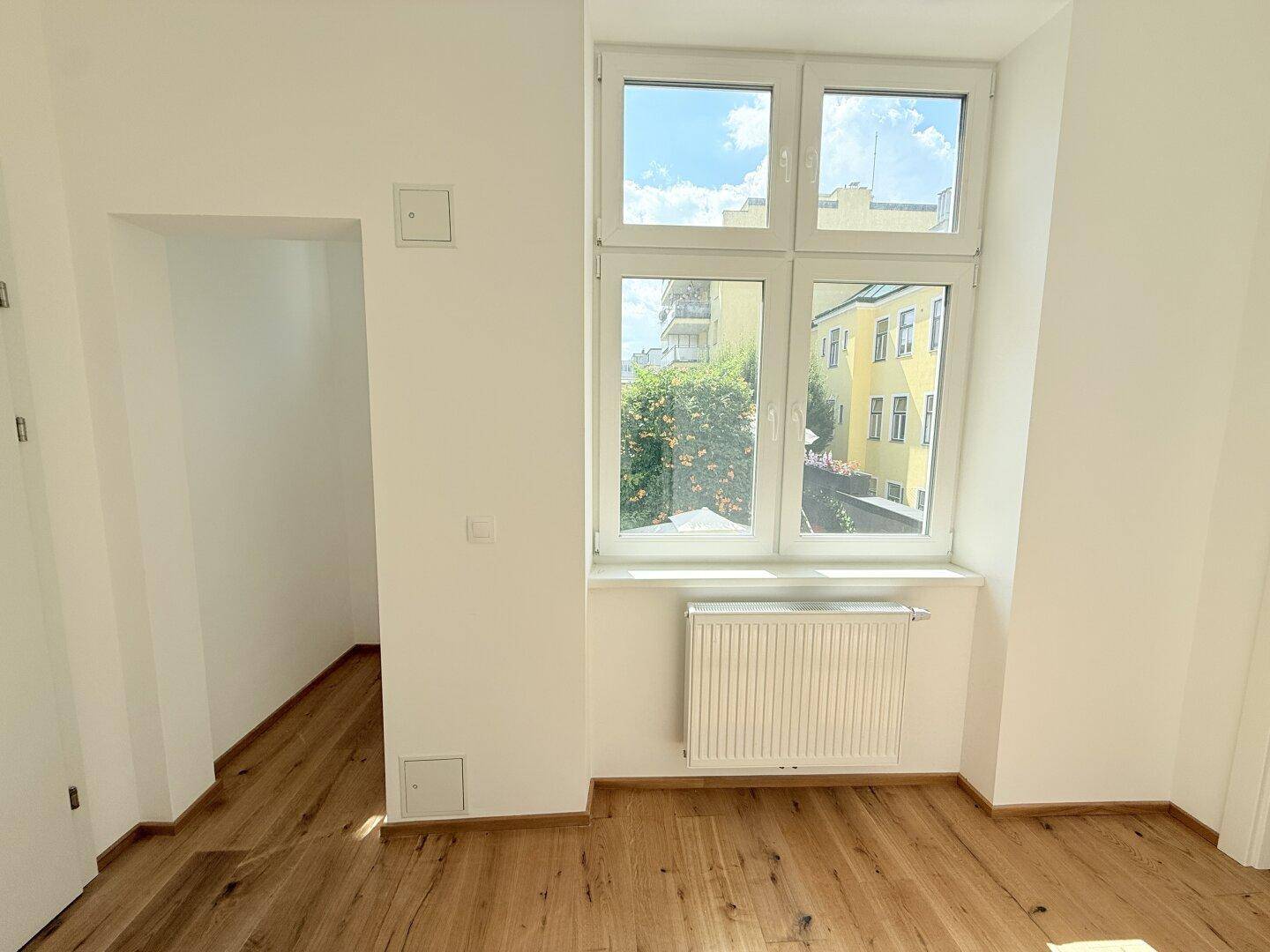 Heller Raum mit Holzboden und großem Fenster, bietet eine kleine Nische.
