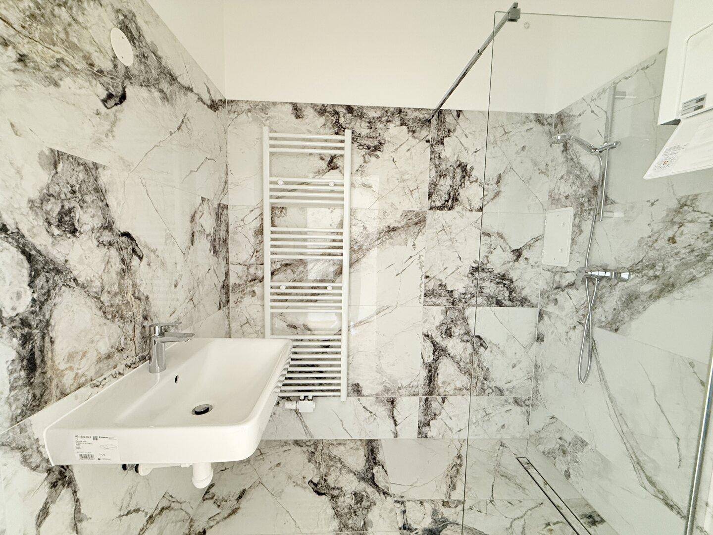 Modernes Badezimmer mit Marmorfliesen, begehbarer Dusche und beheiztem Handtuchhalter.