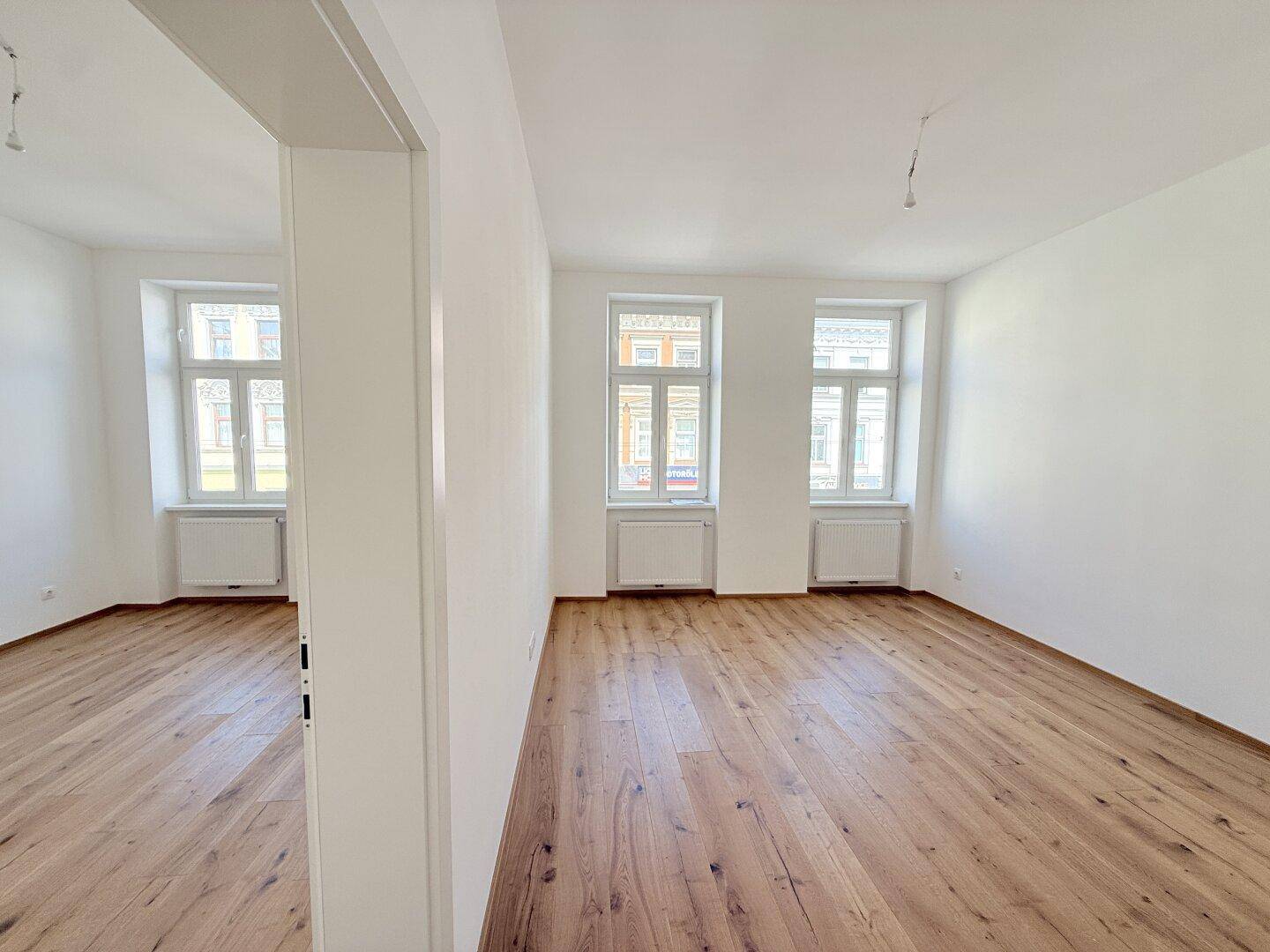 Heller, leerer Raum mit Holzboden und drei großen Fenstern, bereit zur Einrichtung.