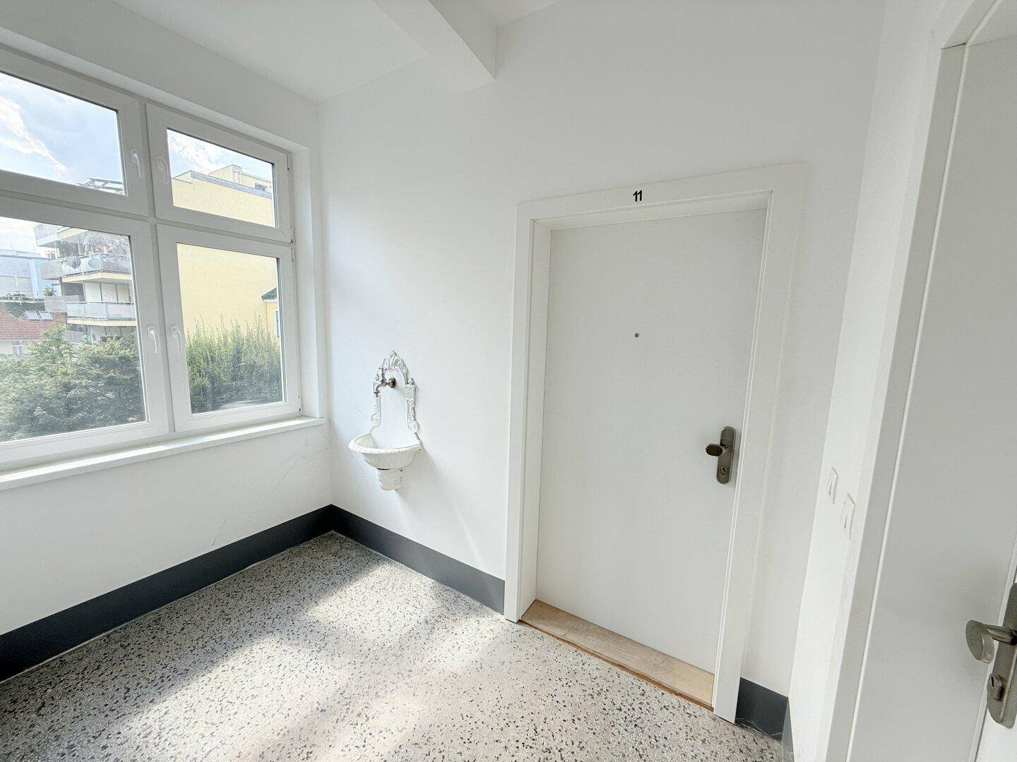 Heller Hausflur mit Terrazzoboden, Fenster und einem dekorativen Wandbrunnen.