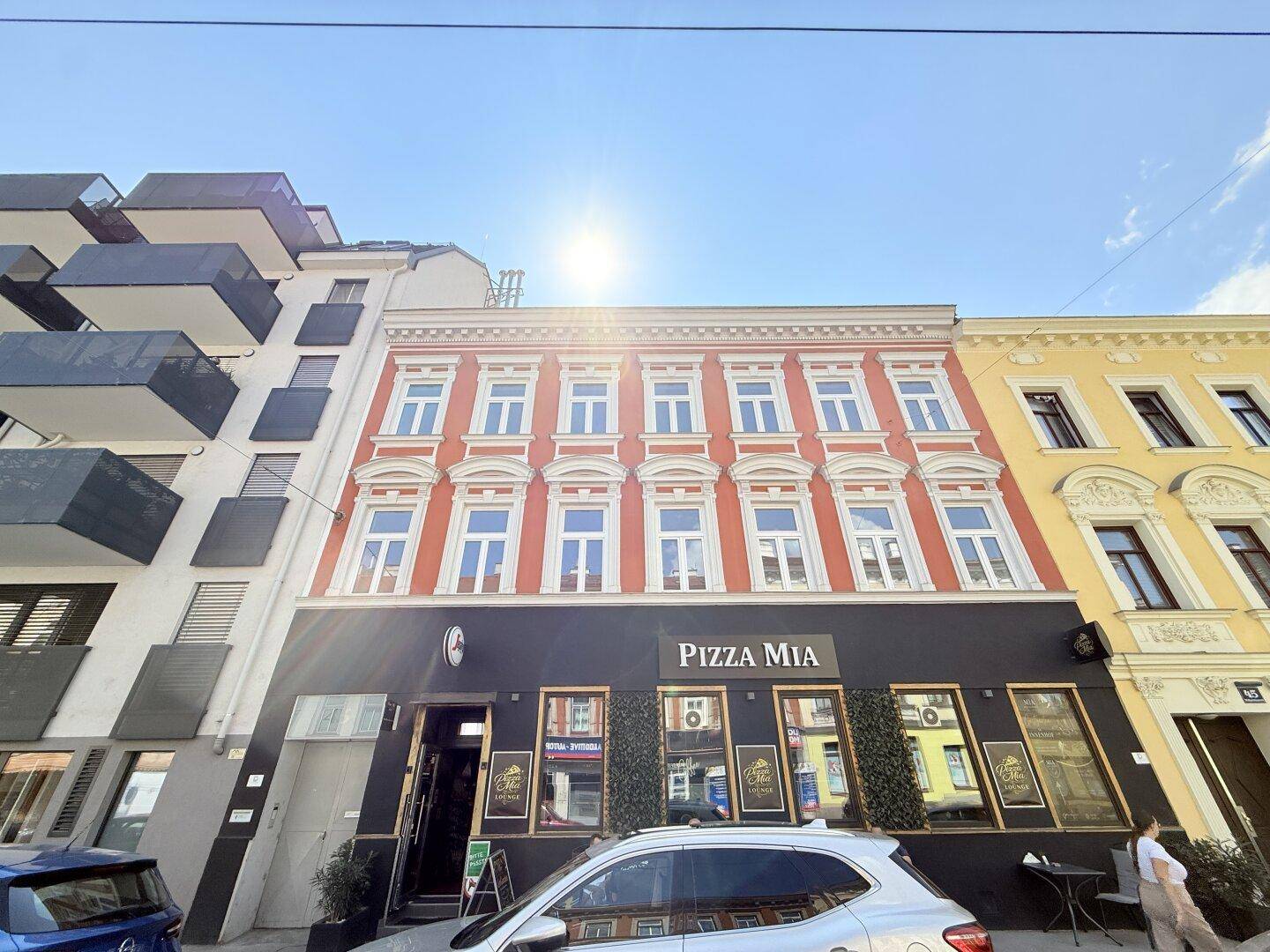 Historische Fassade eines Gebäudes mit roter Farbe, vielen Fenstern und einem Geschäft im Erdgeschoss.