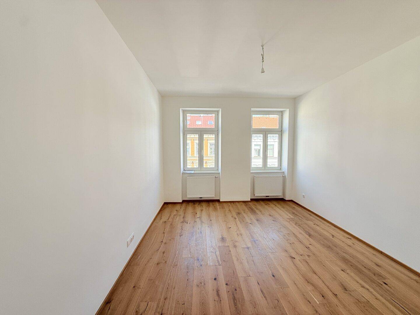 Heller, leerer Raum mit Holzboden und zwei Fenstern, bereit zur individuellen Gestaltung.