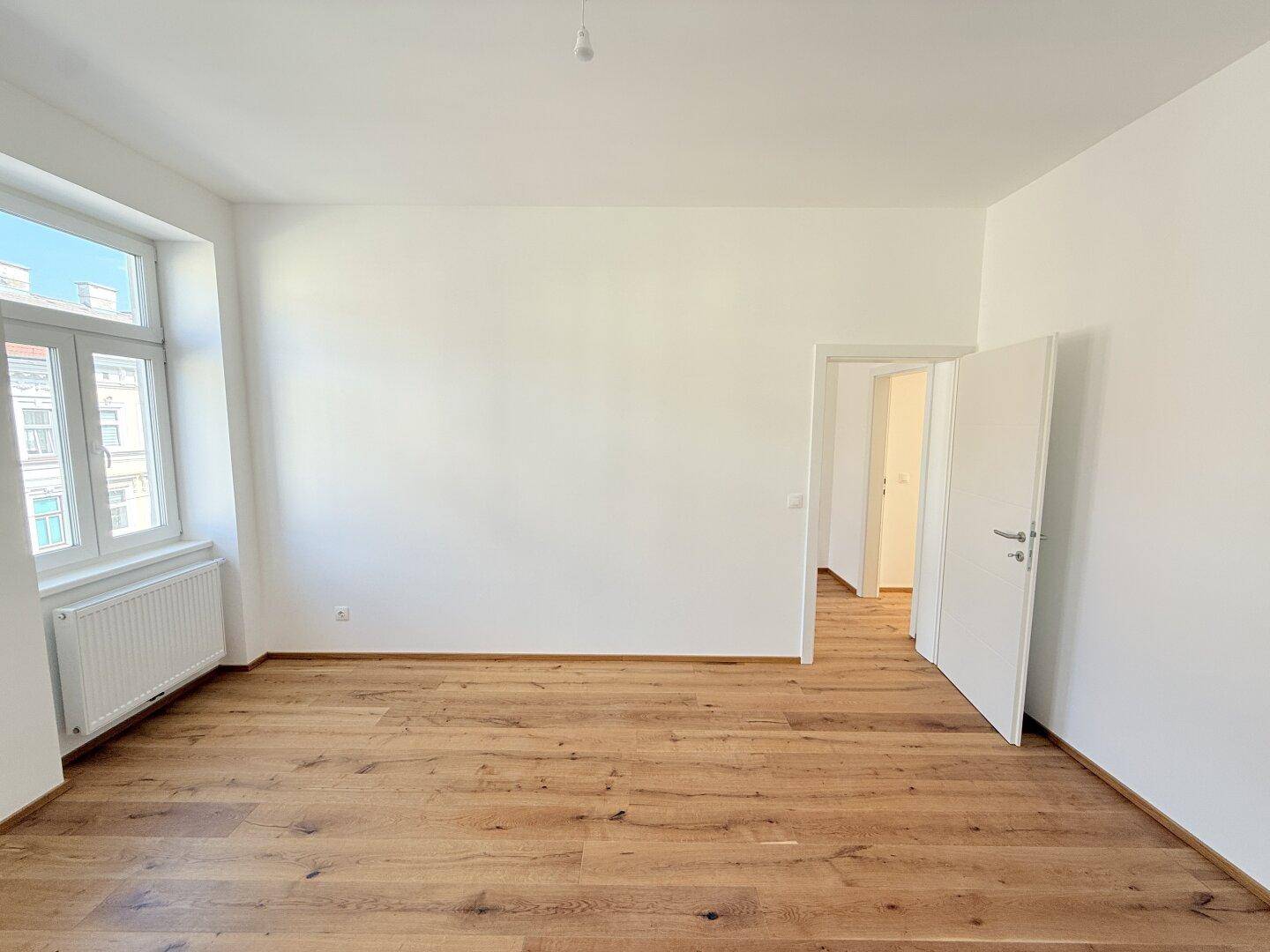 Geräumiger, heller Raum mit Holzboden und Zugang zu weiteren Zimmern, ideal für flexible Nutzung.
