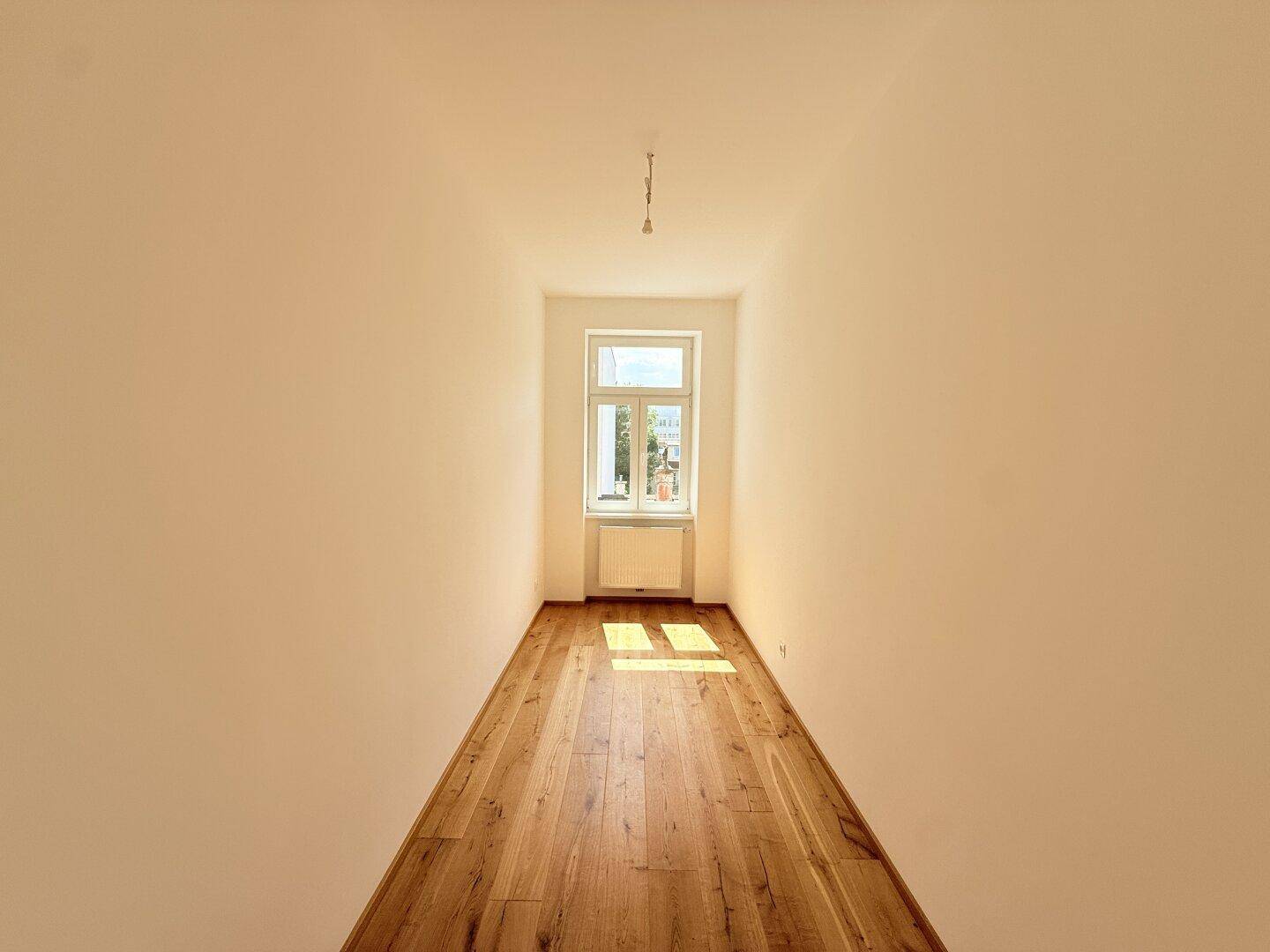Heller, sonniger Raum mit Holzboden und einem Fenster, ideal für ein kleines Büro oder Gästezimmer.