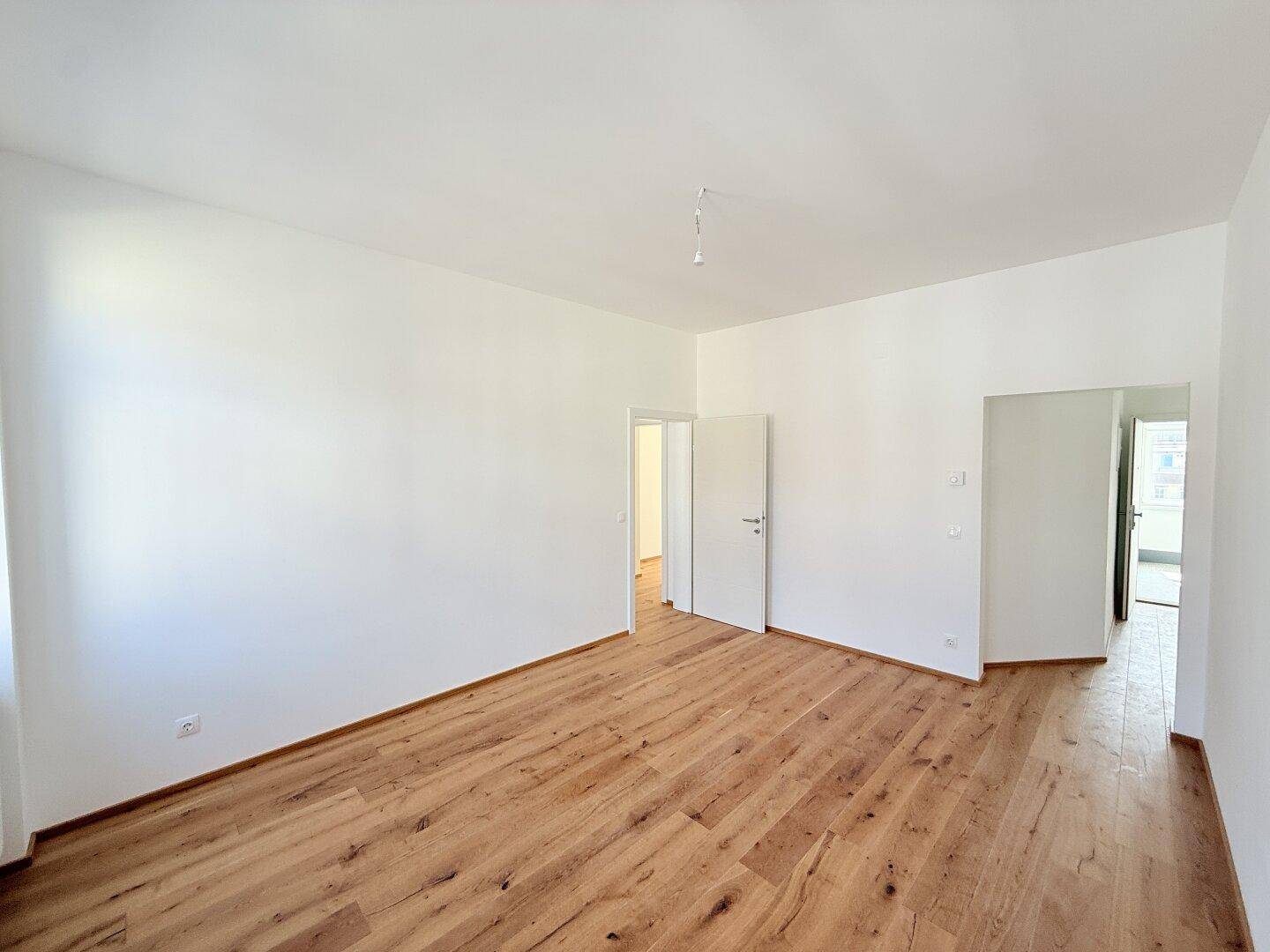 Leerer Raum mit Holzboden und weiß gestrichenen Wänden, vielseitig nutzbar für Wohnzwecke.