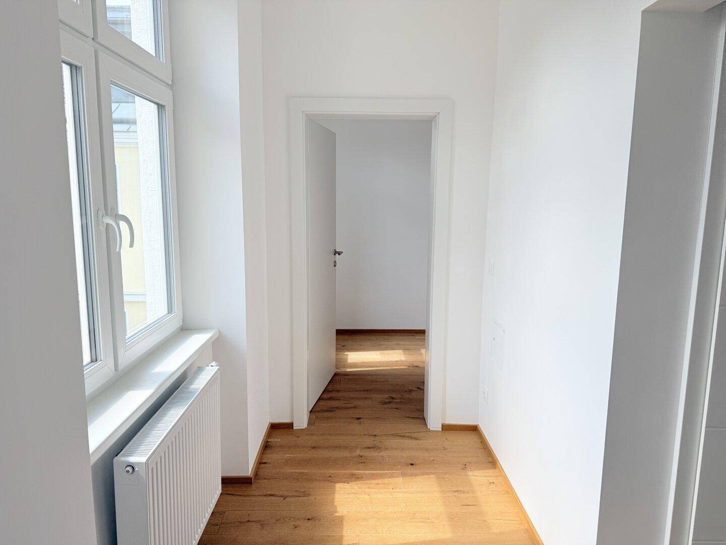 Heller Flur mit Holzboden und Zugang zu weiteren Räumen, gut beleuchtet durch ein Fenster.