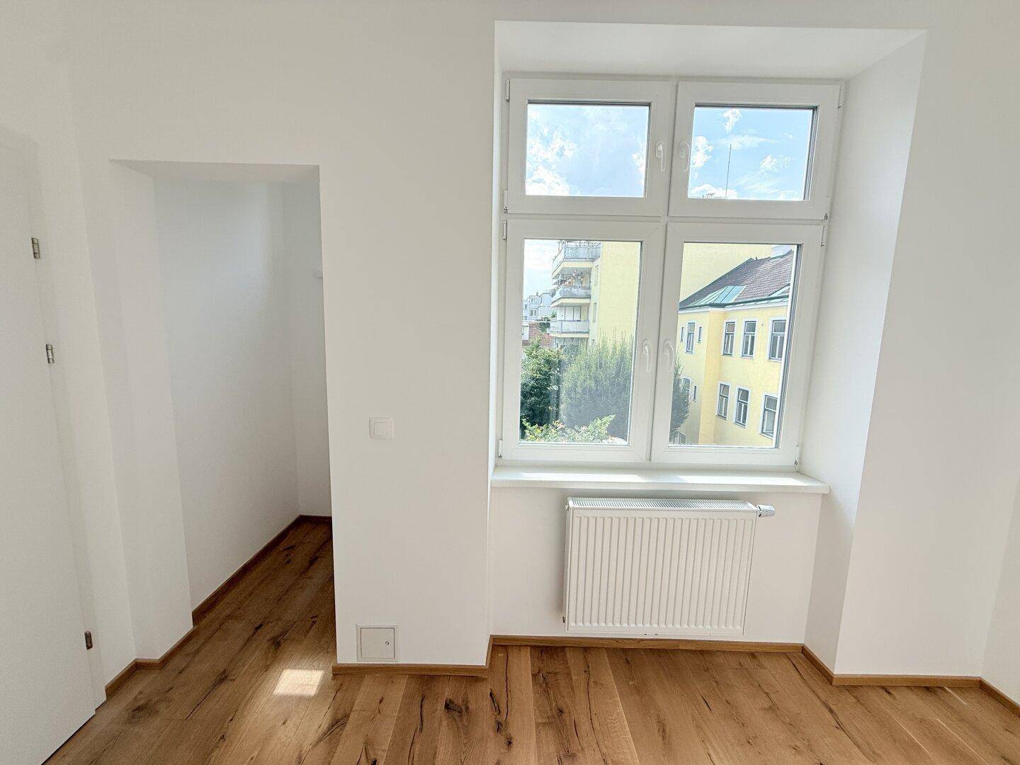 Heller Raum mit Holzboden und großem Fenster, inklusive einer praktischen Nische.