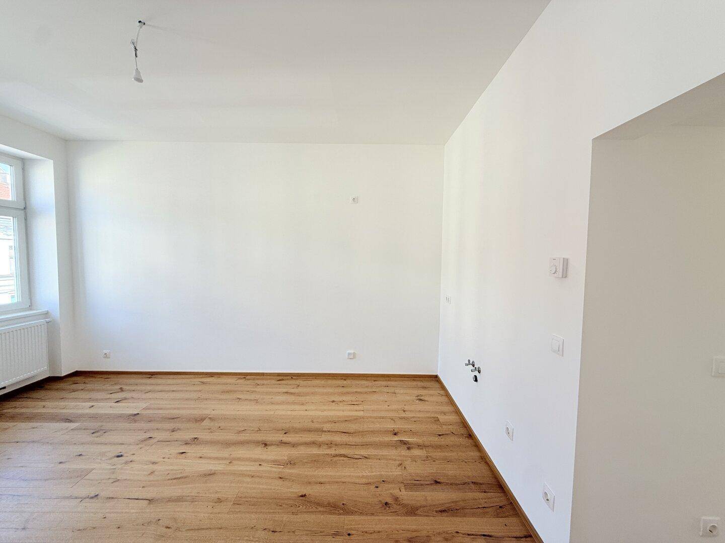 Leerer Raum mit Holzboden und weiß gestrichenen Wänden, ideal für ein Wohnzimmer.