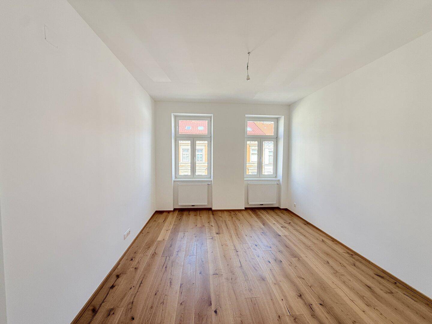 Geräumiger, heller Raum mit Holzboden und zwei Fenstern, bietet viel Gestaltungspotenzial.