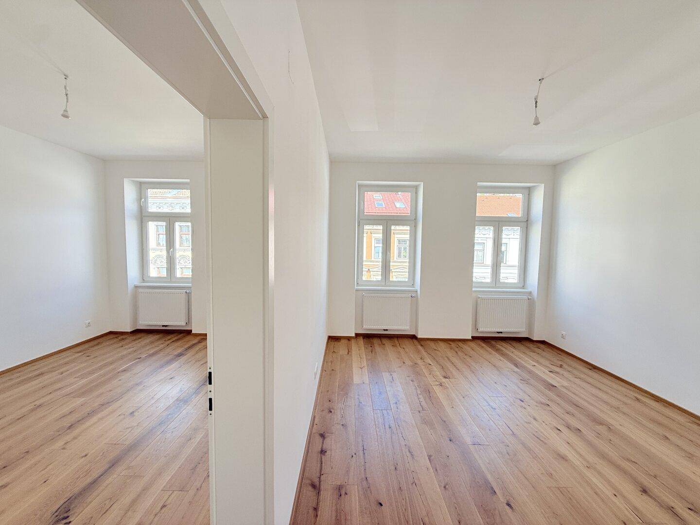 Heller, leerer Raum mit Holzboden und großen Fenstern, bereit zur individuellen Gestaltung.