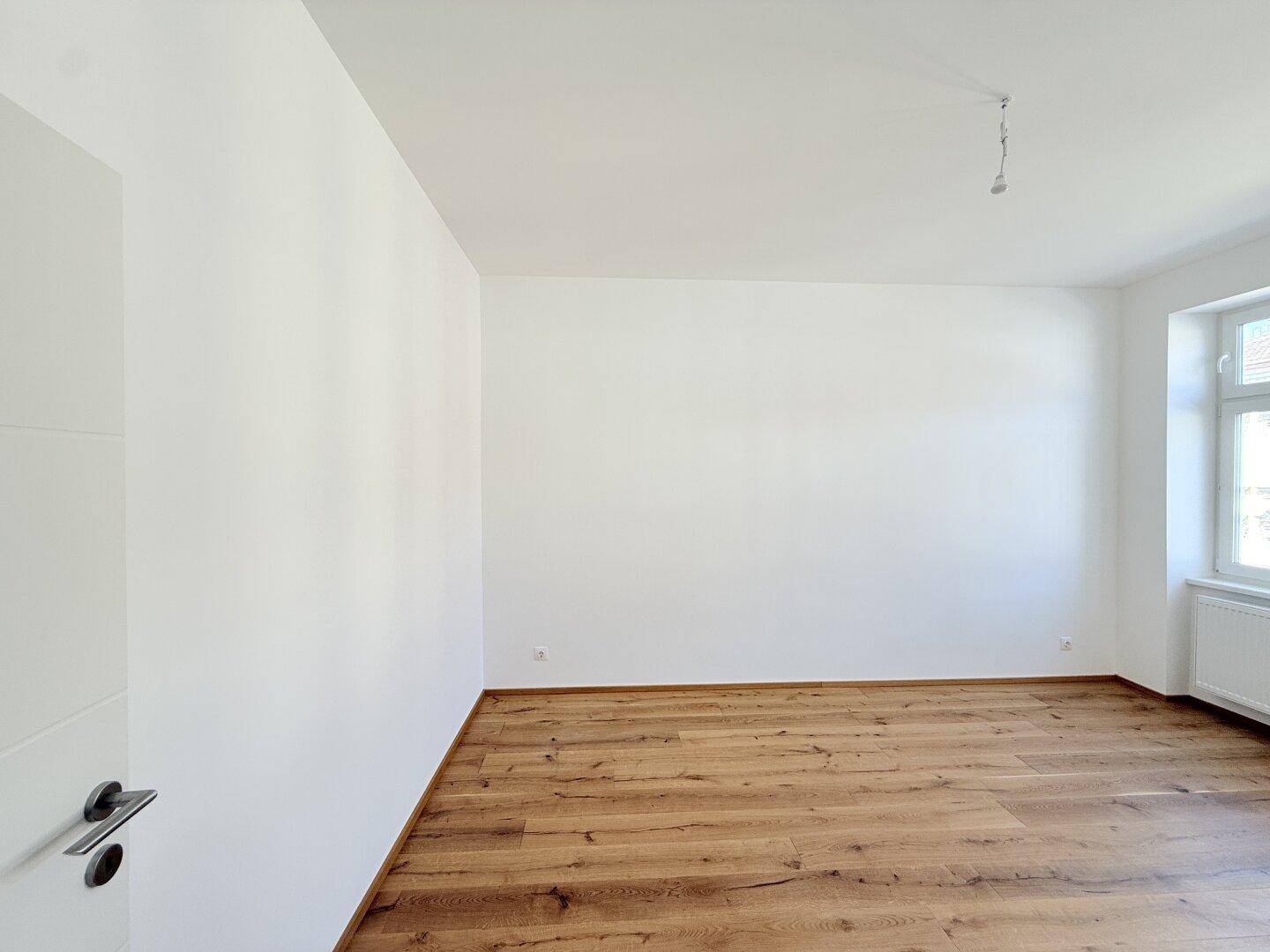 Leerer Raum mit Holzboden und weiß gestrichenen Wänden, bereit für neue Einrichtungsideen.