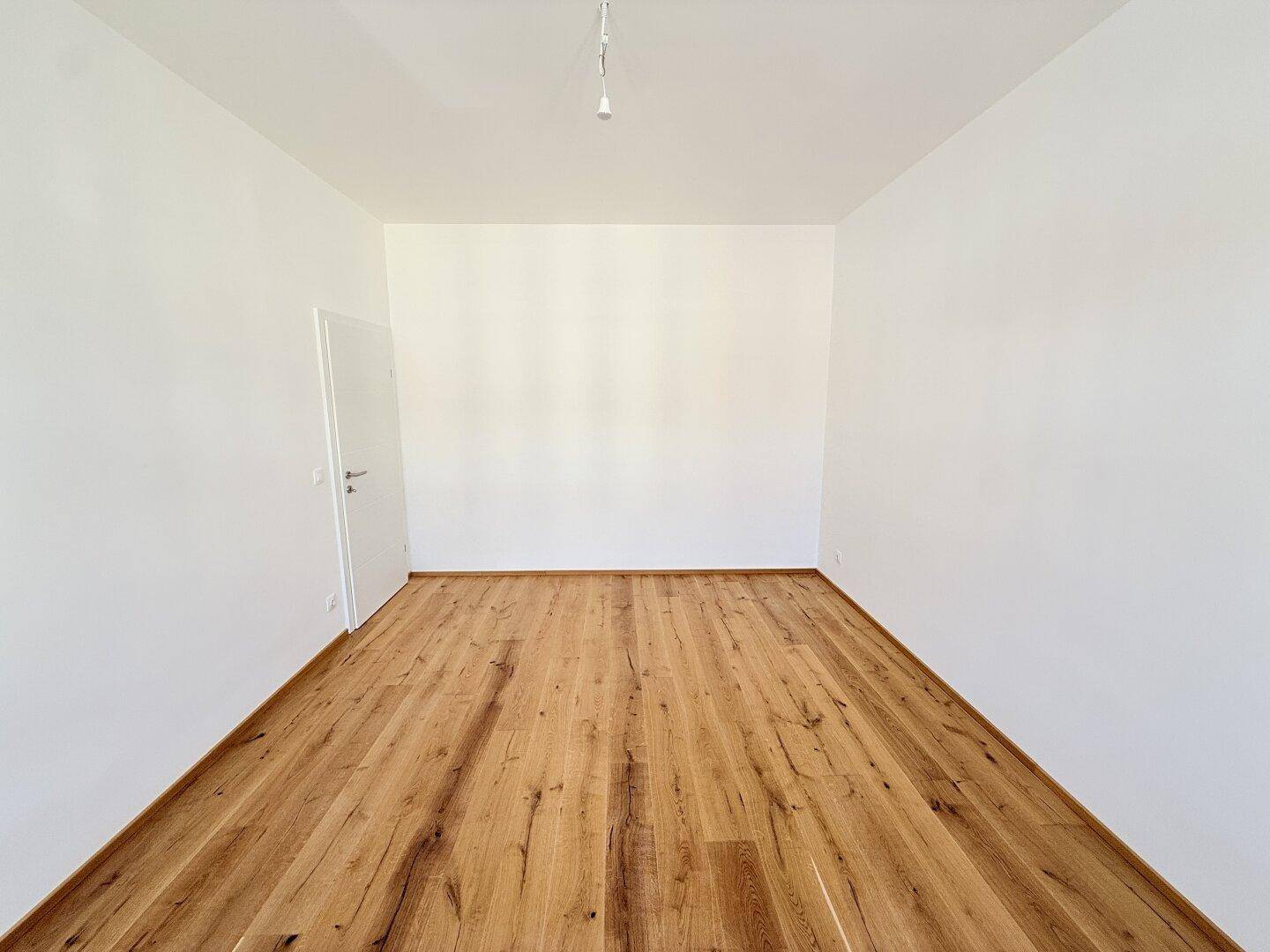 Leerer Raum mit Holzboden und weiß gestrichenen Wänden, geeignet als Schlaf- oder Arbeitszimmer.
