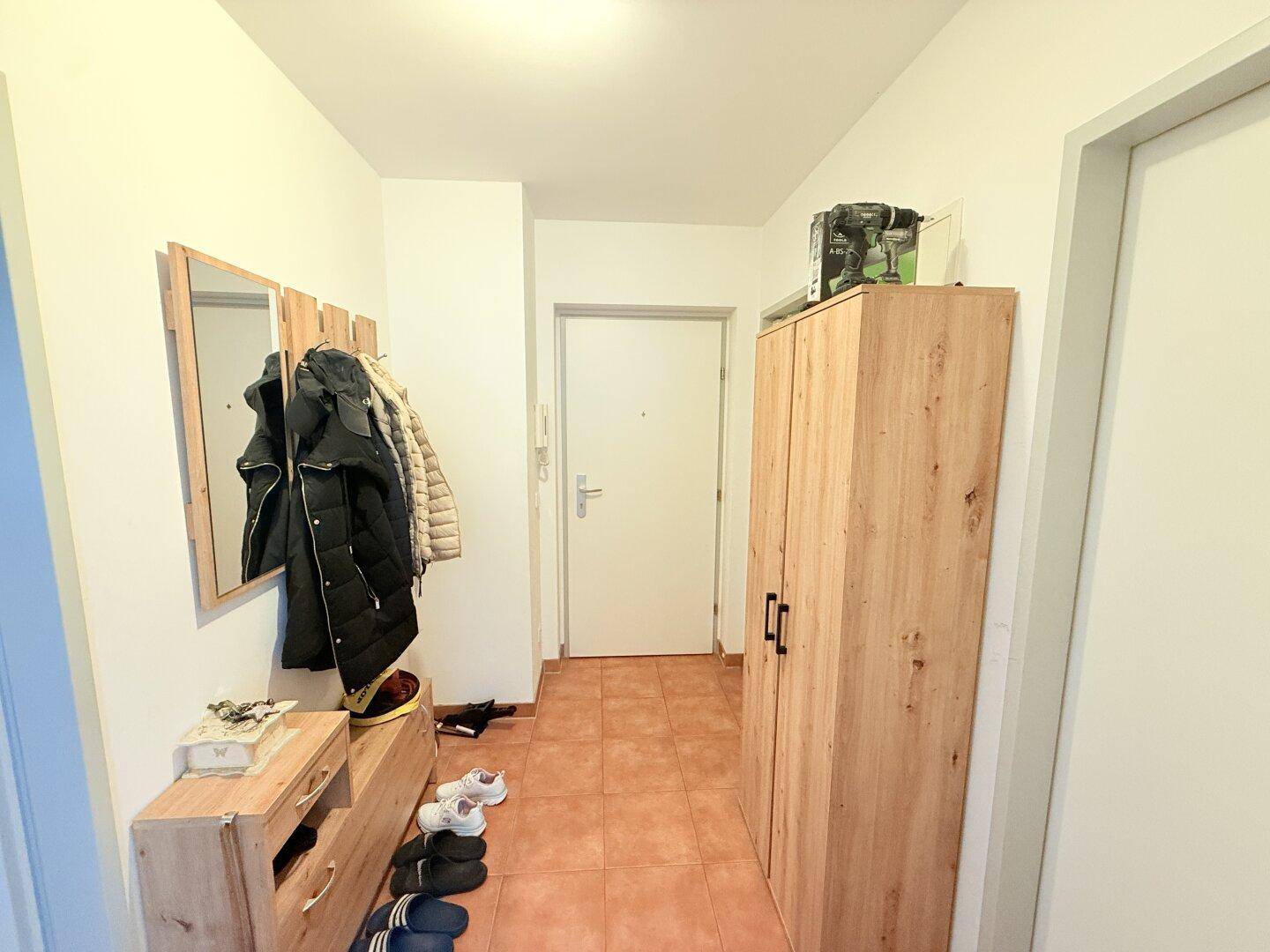 Eingangsbereich mit Fliesenboden, Garderobe und Holzschrank.
