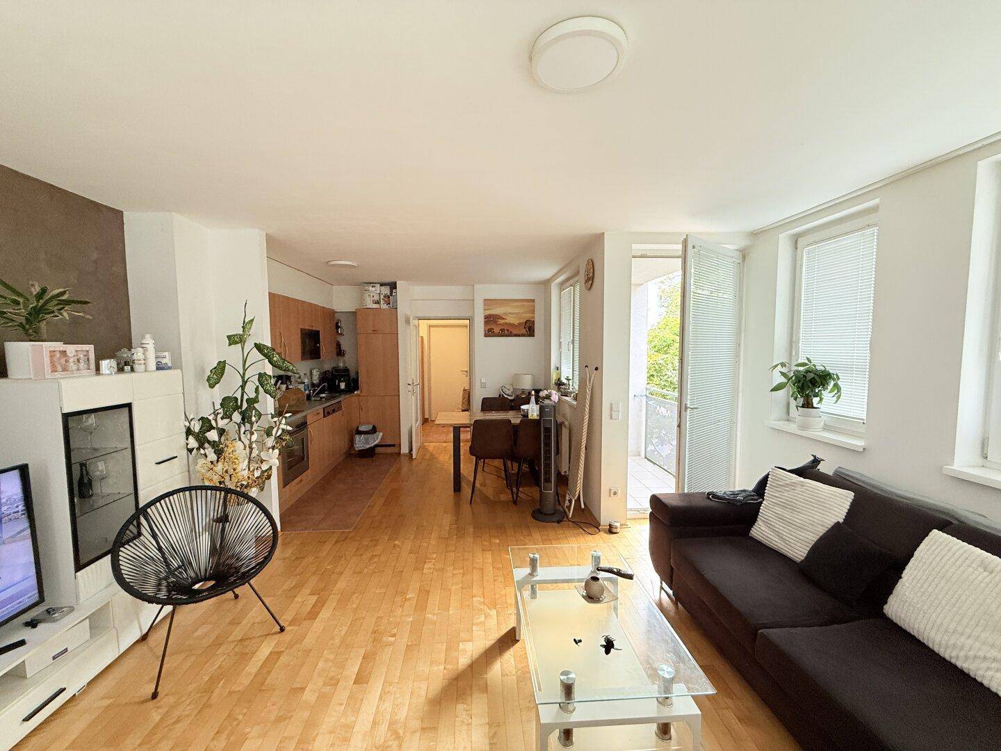 Offener Wohnbereich mit Holzboden, Essbereich und Zugang zum Balkon.
