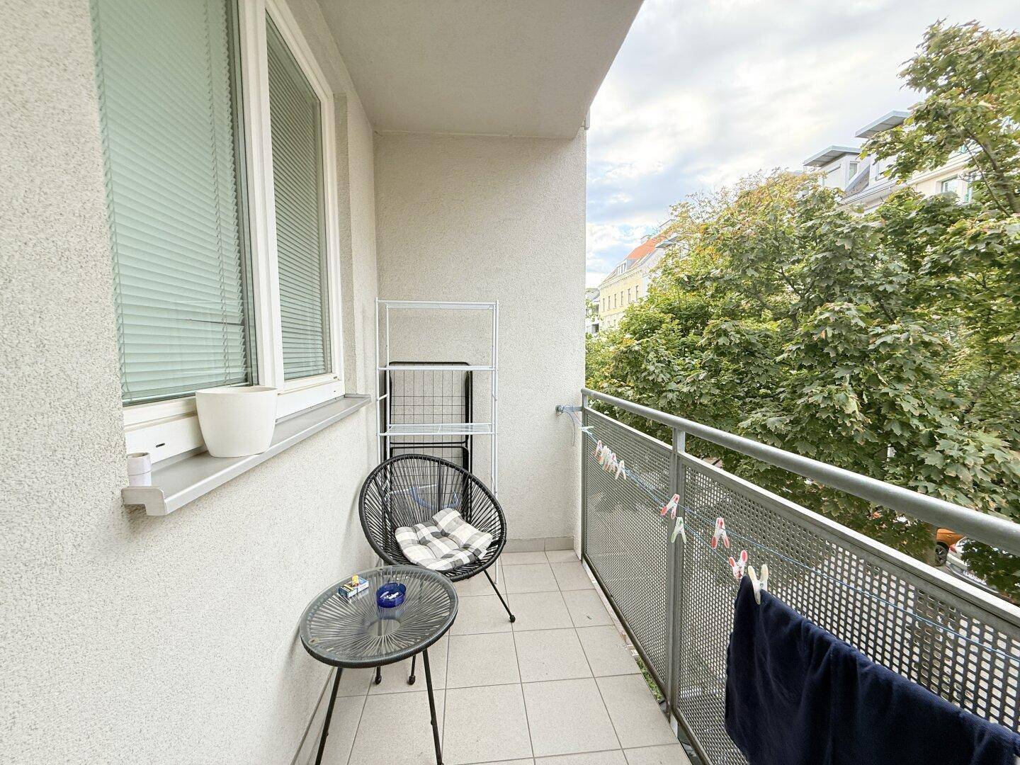 Kleiner Balkon mit Fliesenboden, Sitzgelegenheit und Blick ins Grüne.