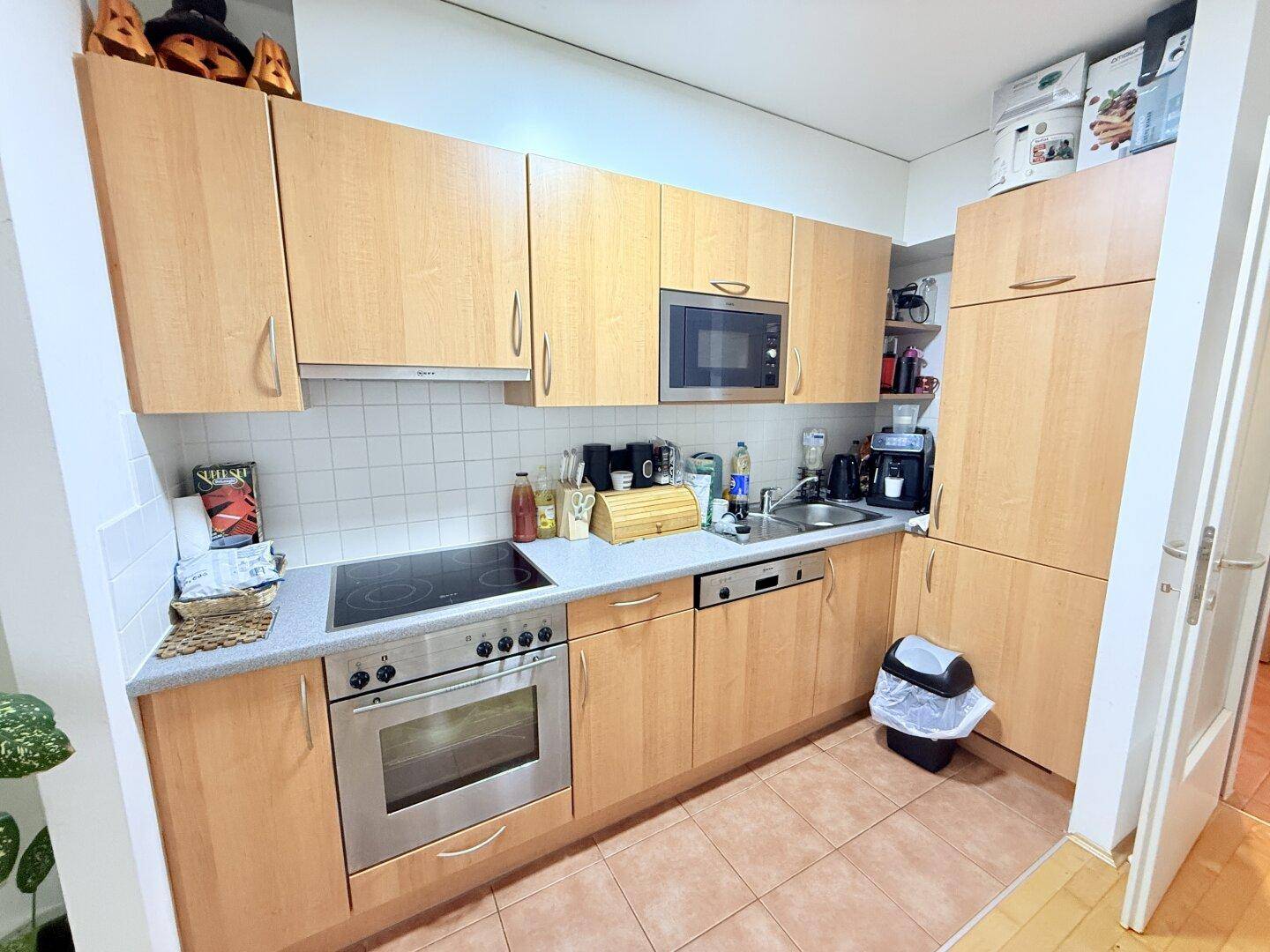 Helle Einbauküche mit Holzfronten, Fliesenboden und modernen Küchengeräten.