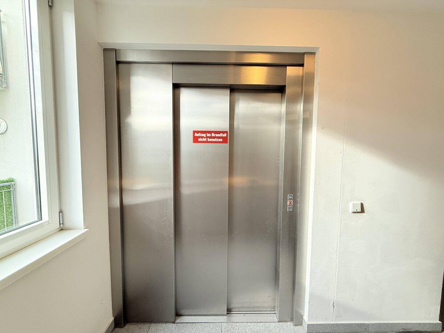 Moderner Aufzug im Gebäude mit Edelstahltüren und Hinweisschild.