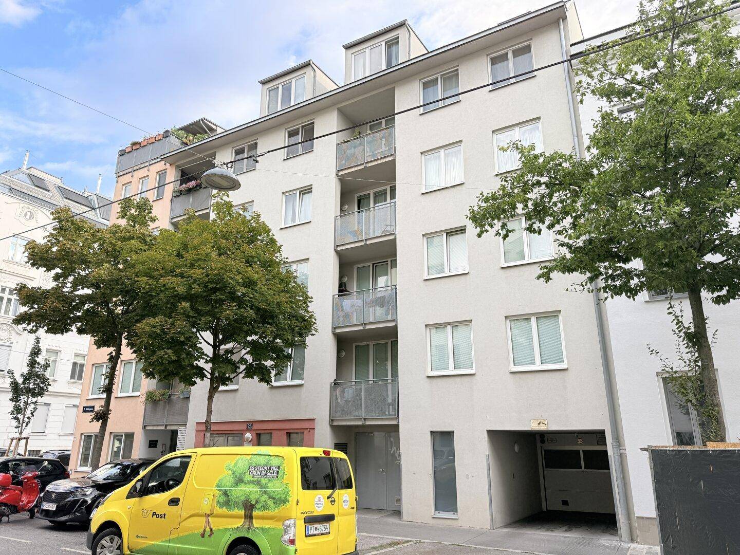 Mehrfamilienhaus mit Balkonen, großen Fenstern und Parkplätzen an der Straße.
