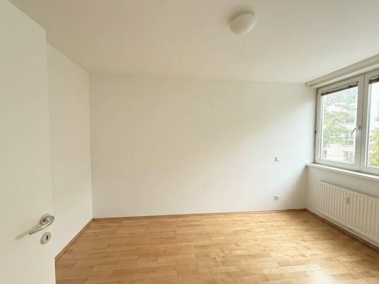 Geräumiges Schlafzimmer mit Holzboden, weißen Wänden und großem Fenster.