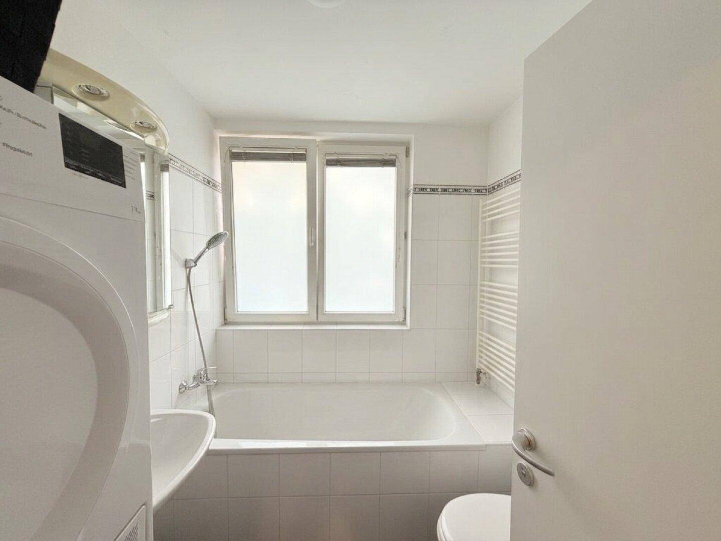 Badezimmer mit Badewanne, Waschbecken, Fenster und Waschmaschine.