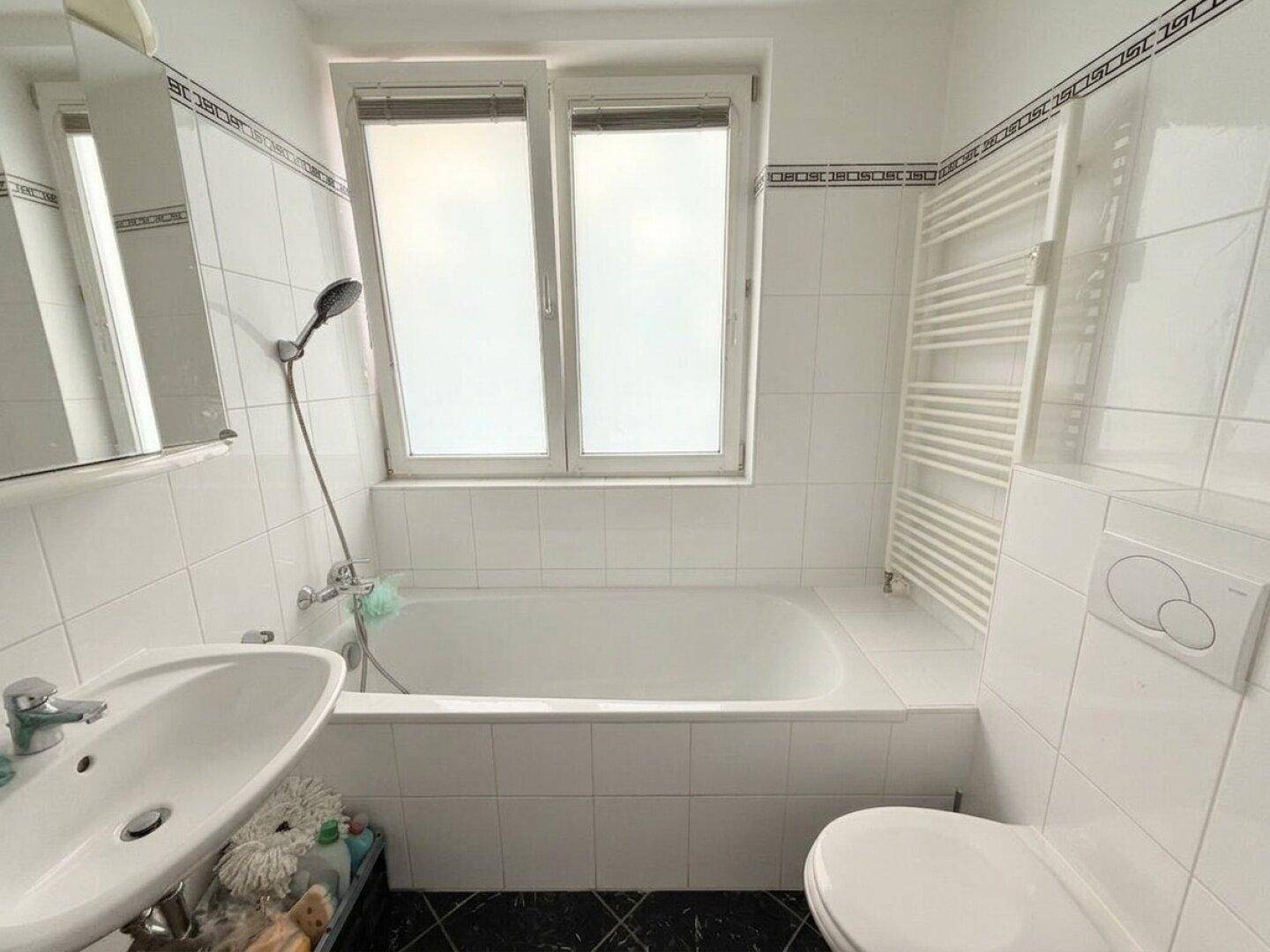 Gefliestes Badezimmer mit Badewanne, WC, Waschbecken und Fenster.