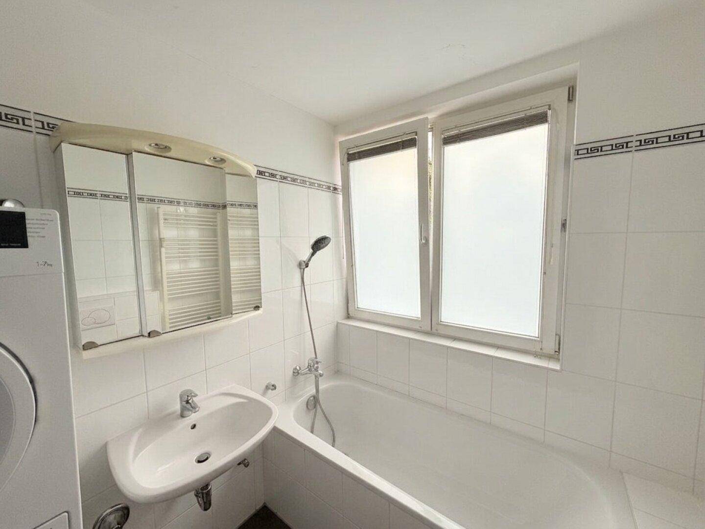 Helles Badezimmer mit Badewanne, Waschbecken, Spiegelschrank und Fenster.