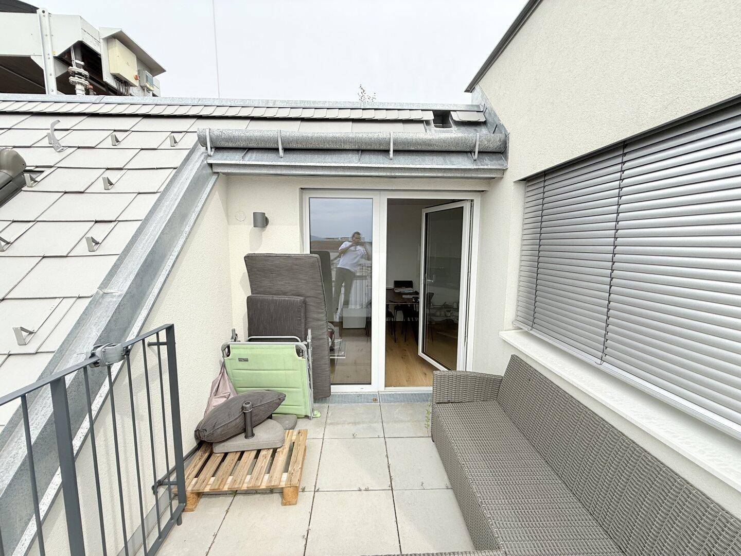 Balkon mit Outdoor-Sofa und Blick auf das Dach des Gebäudes und die Umgebung.