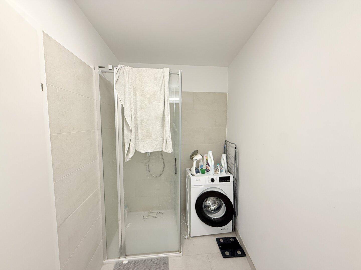 Badezimmer mit Duschkabine und Waschmaschine, teilweise gefliest.