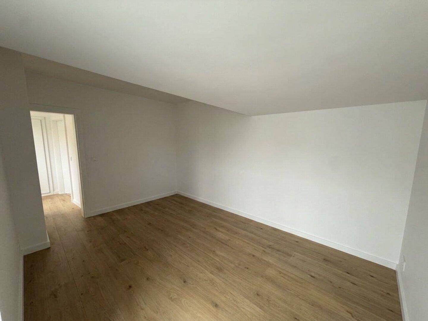 Leeres Schlafzimmer mit Holzboden, weißen Wänden und einer Dachschräge.
