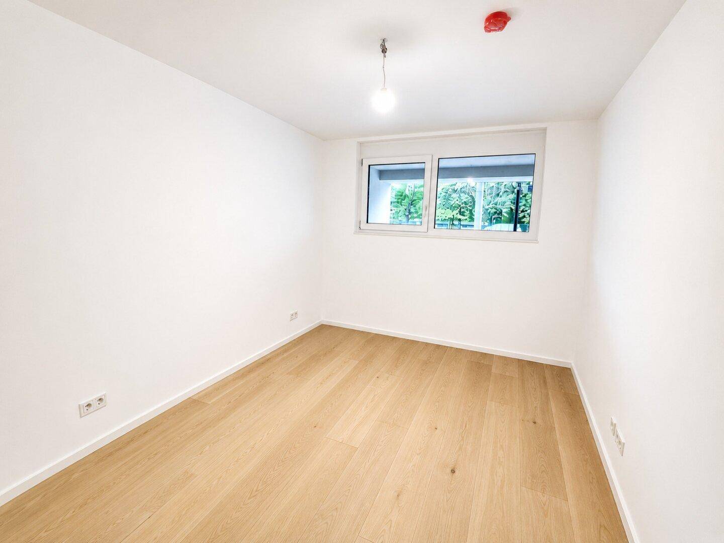 Leeres Schlafzimmer mit hellem Holzboden und einem Fenster, das für natürliche Belichtung sorgt.