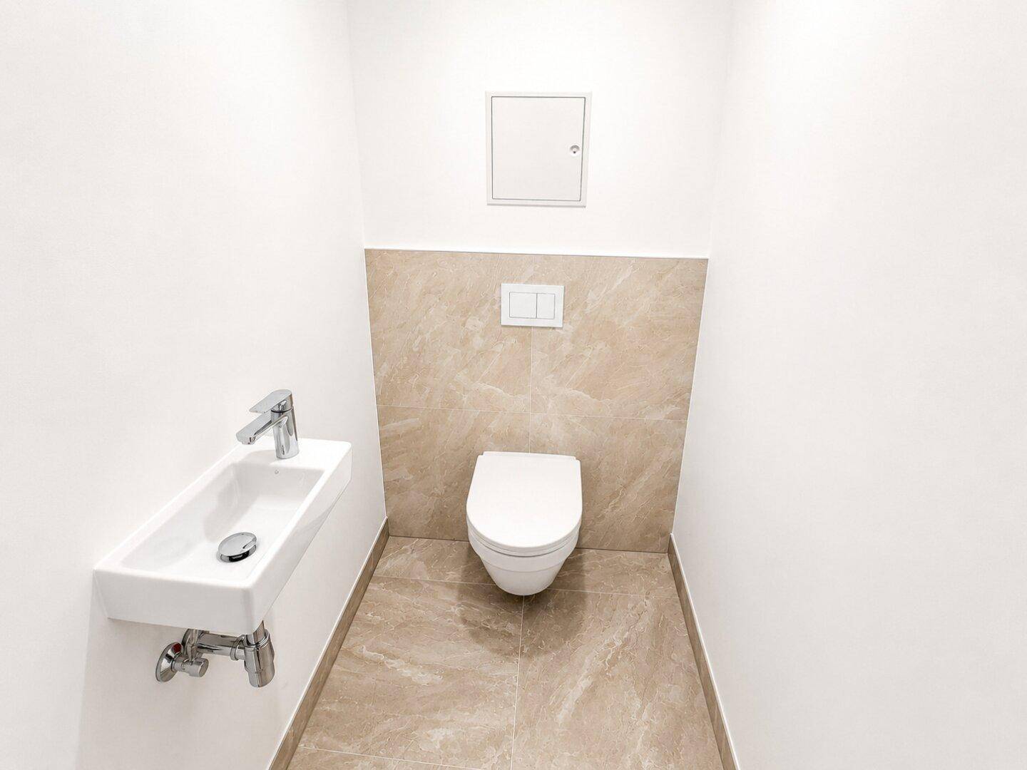 Gäste-WC mit wandhängender Toilette und kleinem Waschbecken, in neutralen Farbtönen gehalten.