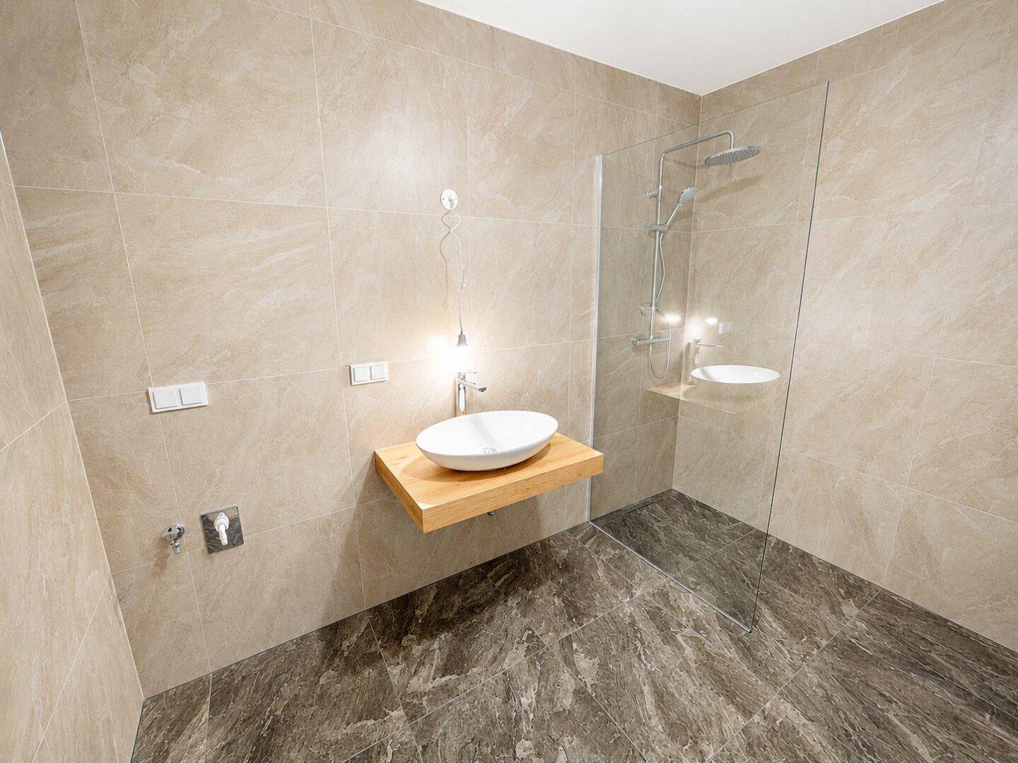 Modernes Badezimmer mit begehbarer Dusche, stilvollem Waschbecken und beigen Wand- und Bodenfliesen.