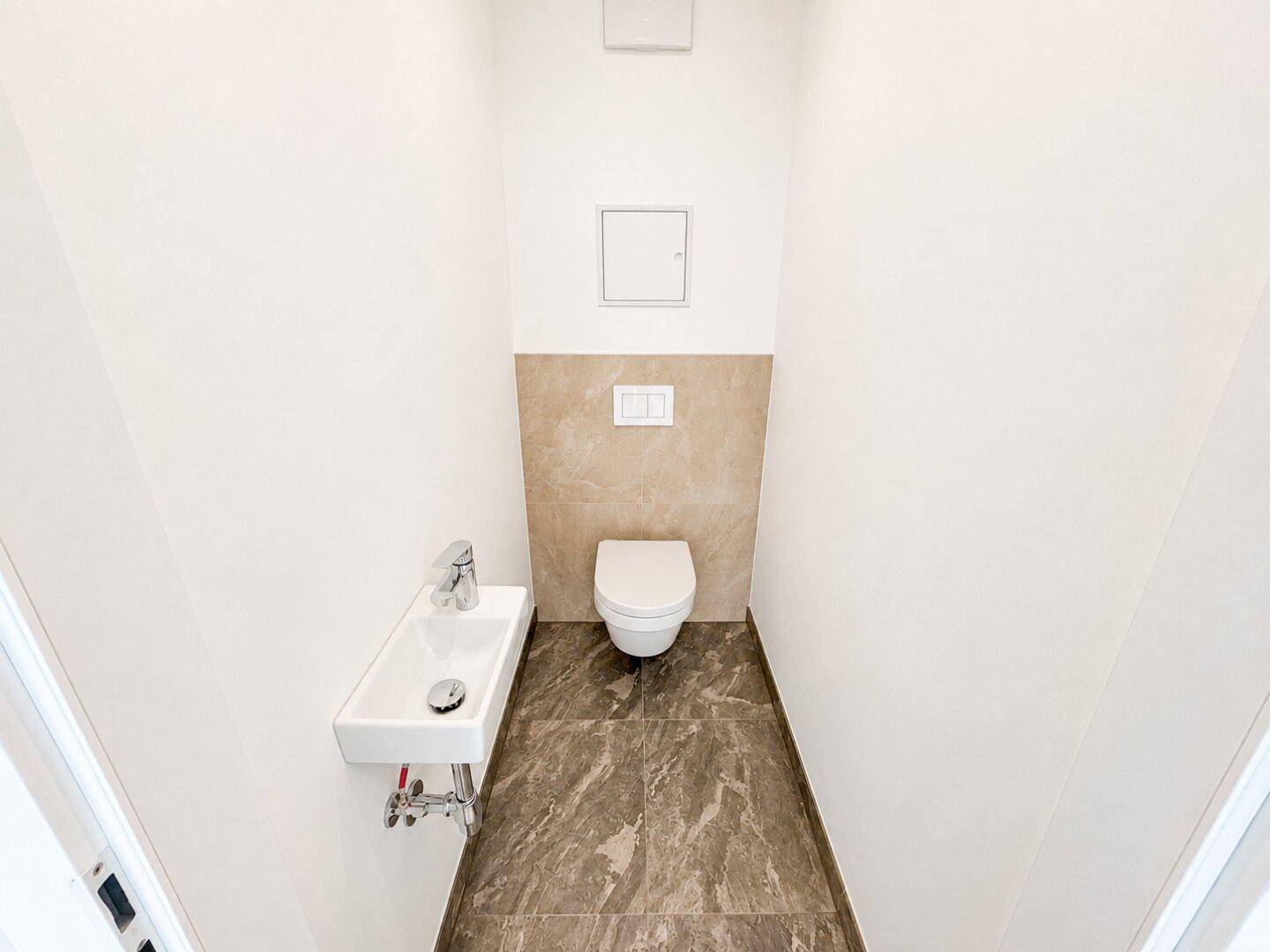Kleines Gäste-WC mit wandhängender Toilette, kleinem Waschbecken und modernen Fliesen.