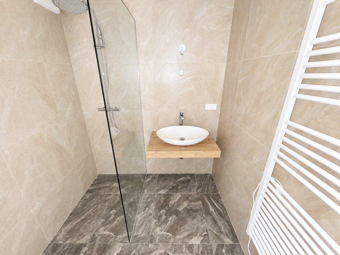 Modernes Badezimmer mit begehbarer Dusche, stilvollem Aufsatzwaschbecken und Handtuchheizkörper.