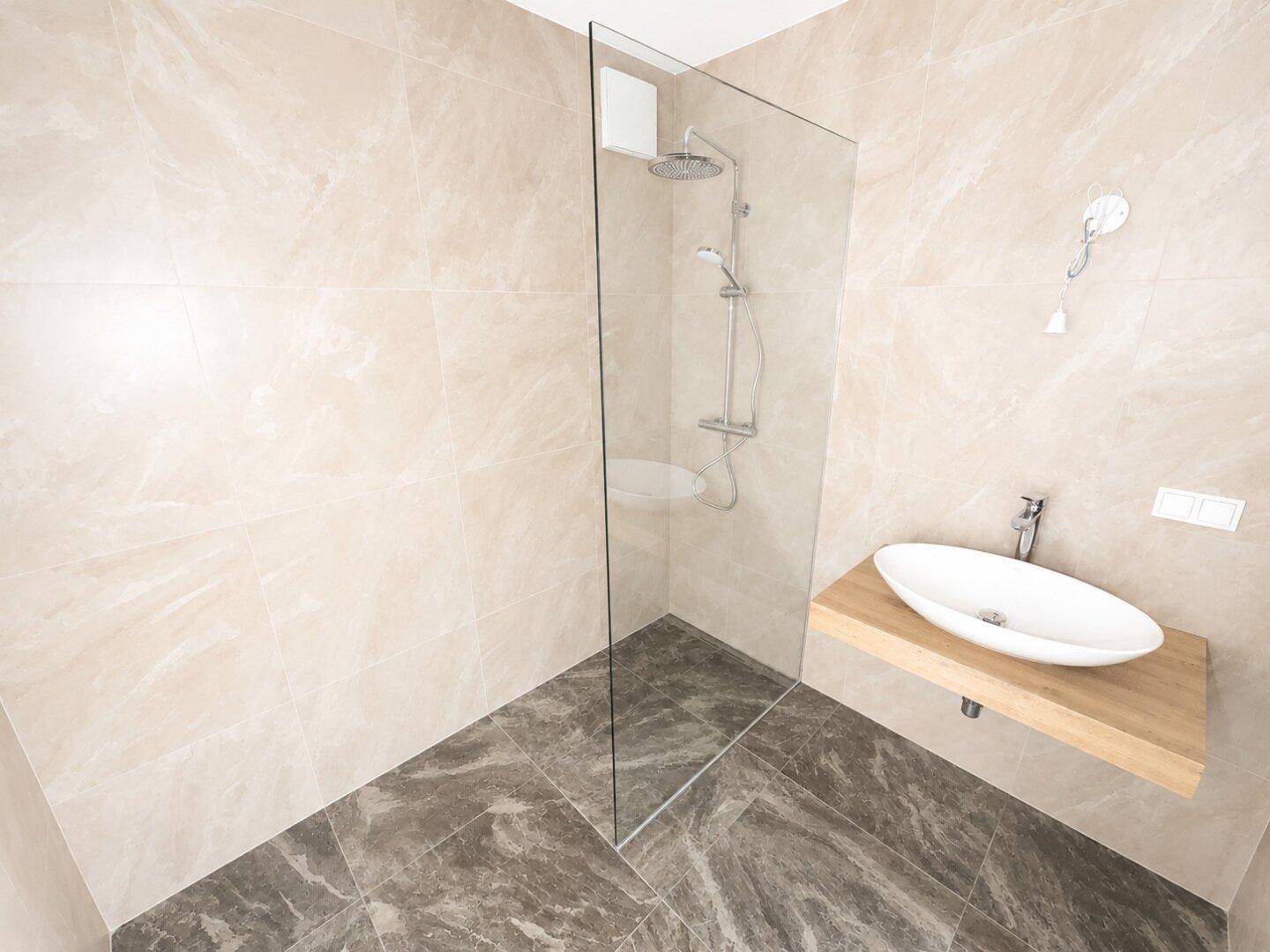 Elegantes Badezimmer mit großformatigen Fliesen, Glasdusche und modernem Holzwaschtisch.