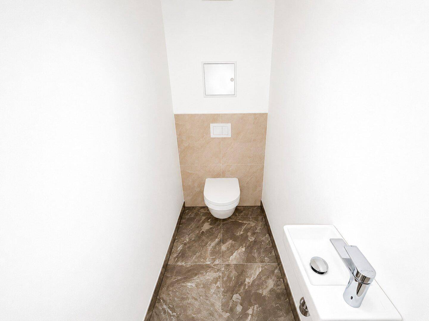 Kompaktes Gäste-WC mit wandhängender Toilette und kleinem Handwaschbecken auf Fliesenboden.