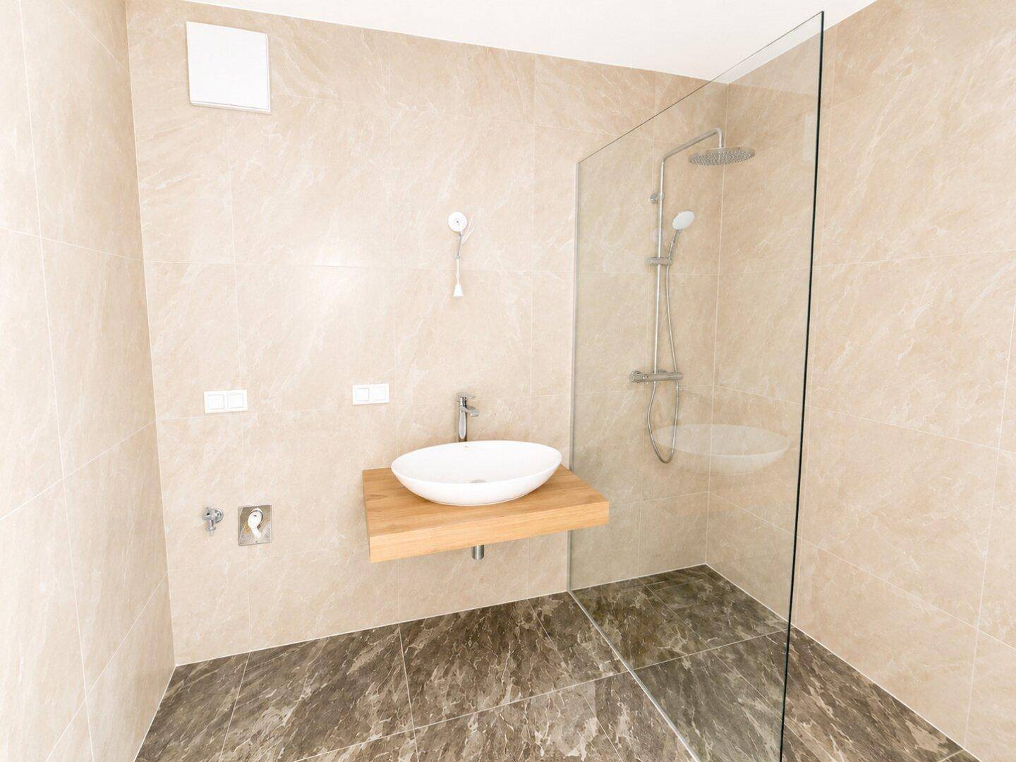 Modernes Badezimmer mit begehbarer Dusche, Waschbecken und beigefarbenen Fliesen.