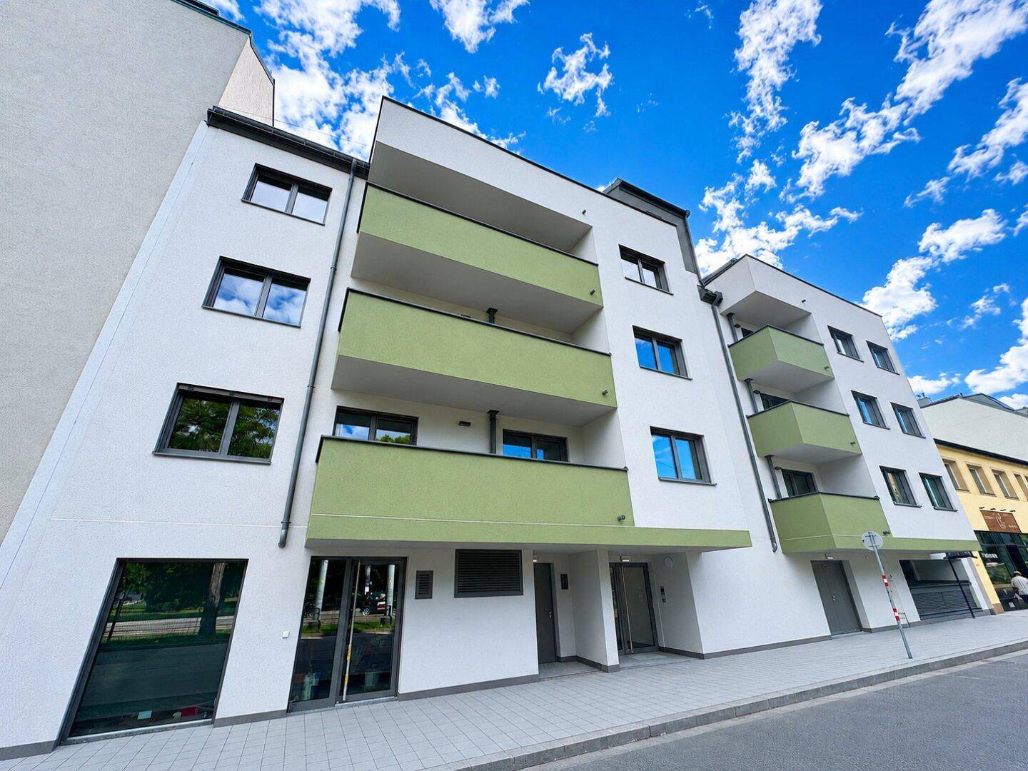 Ansicht eines modernen Mehrfamilienhauses mit weißer Fassade und grünen Balkonen.