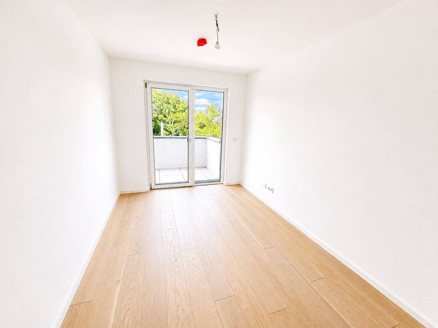 Lichtdurchflutetes Schlafzimmer mit Holzboden und direktem Balkonzugang.