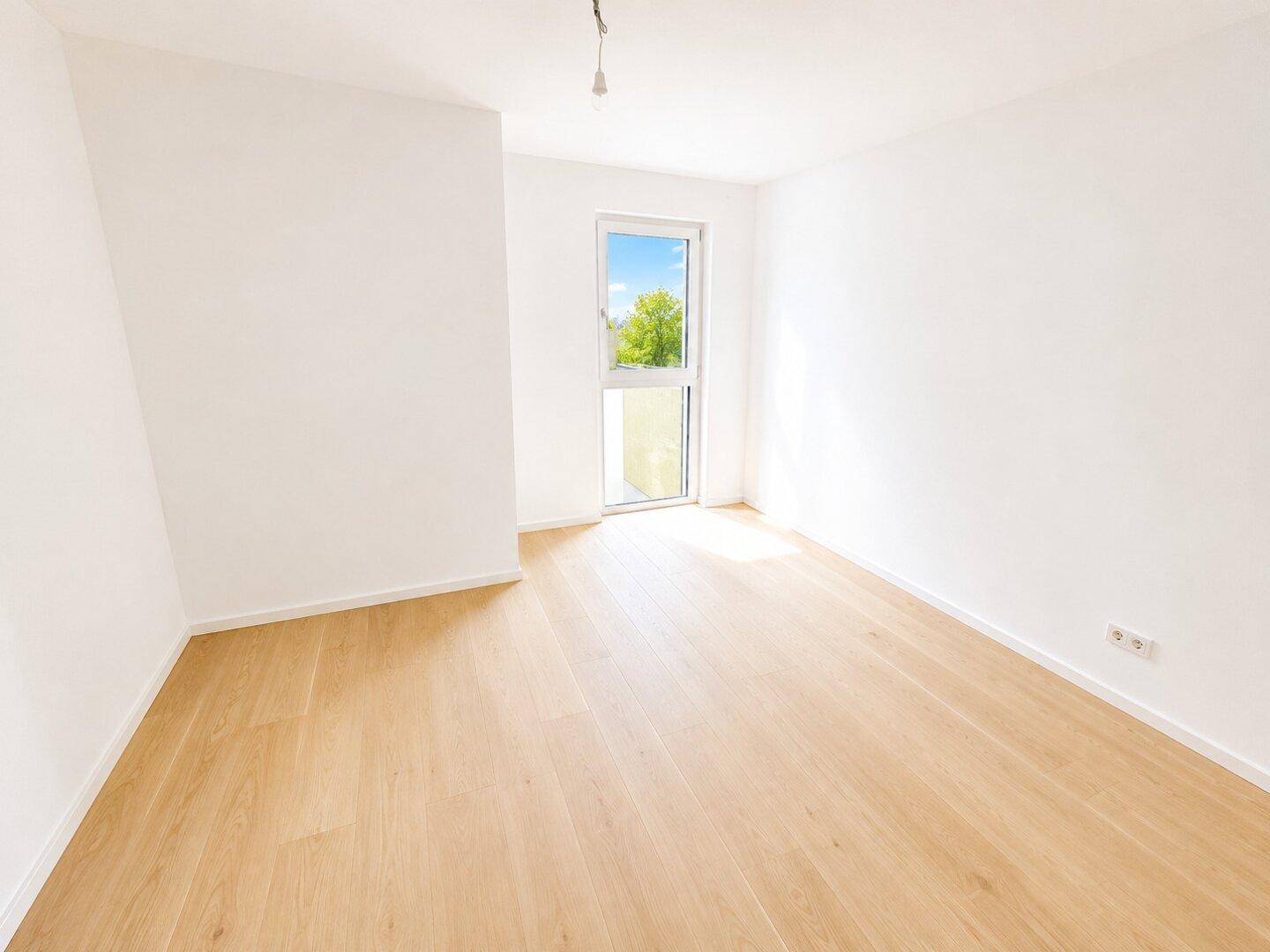 Lichtdurchflutetes Schlafzimmer mit hellem Holzparkett und einem großen Fenster mit Grünblick.