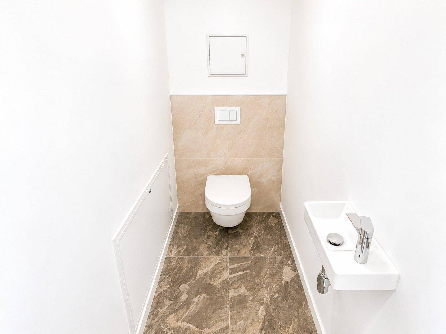 Kompaktes Gäste-WC mit Wand-WC, kleinem Waschbecken und modernen Fliesen.