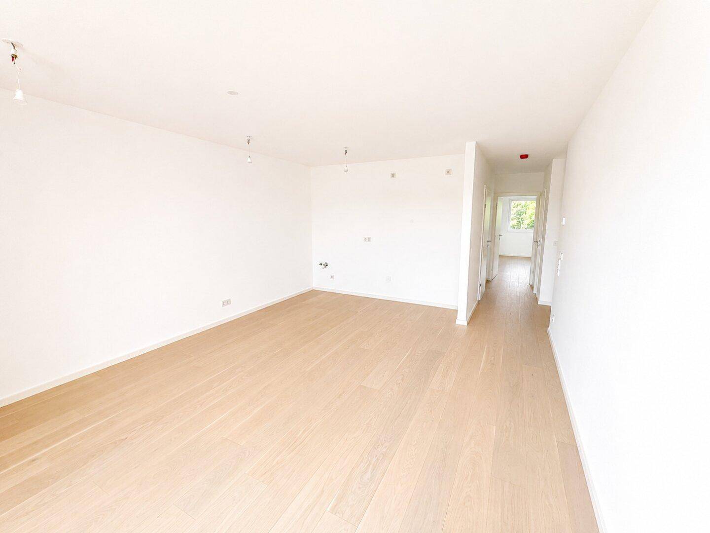 Geräumiges, unmöbliertes Zimmer mit hellem Holzparkett und Zugang zum Flur.