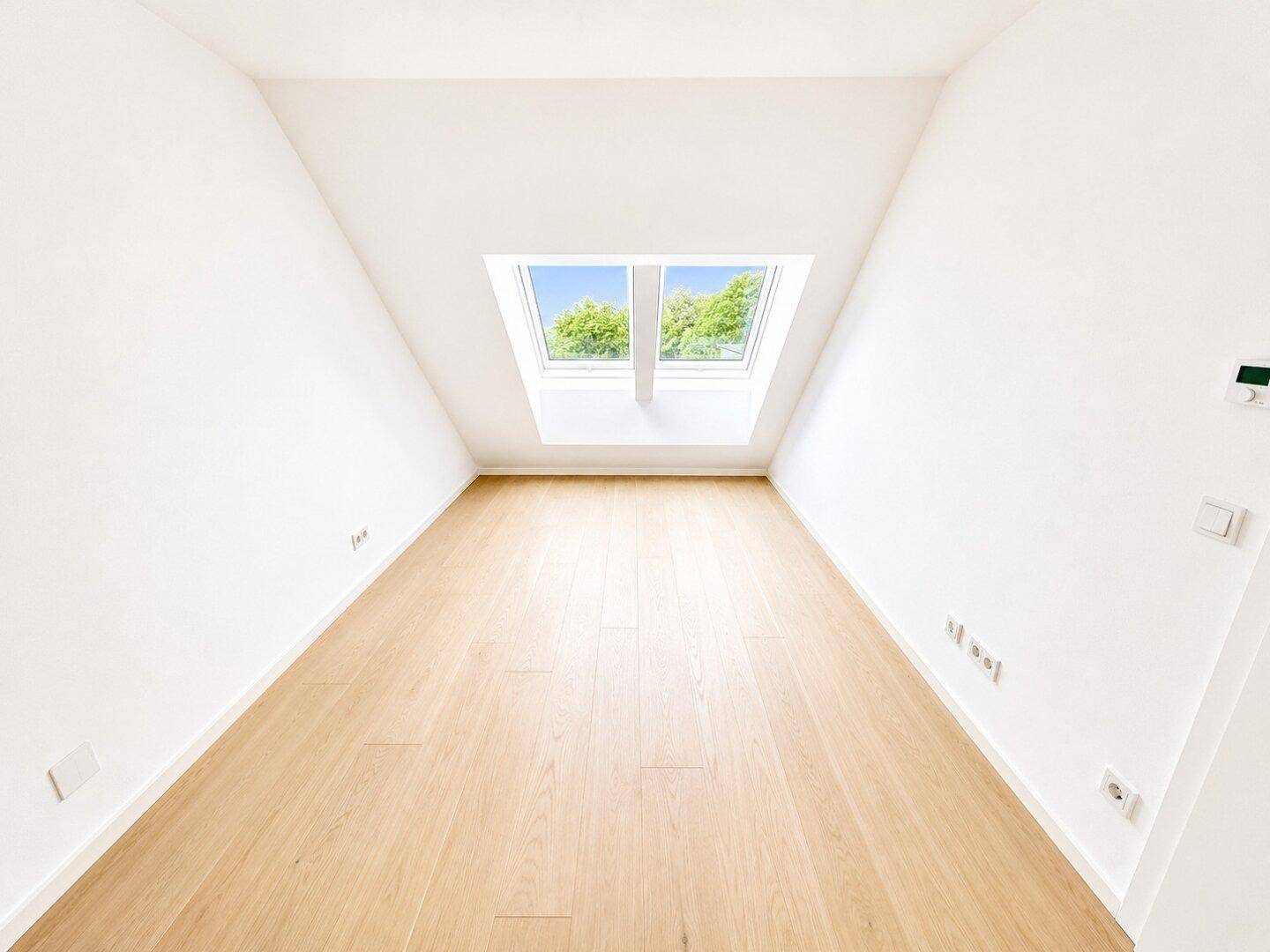 Heller Raum im Dachgeschoss mit Holzboden und zwei großen Dachfenstern, ideal als Schlafzimmer.