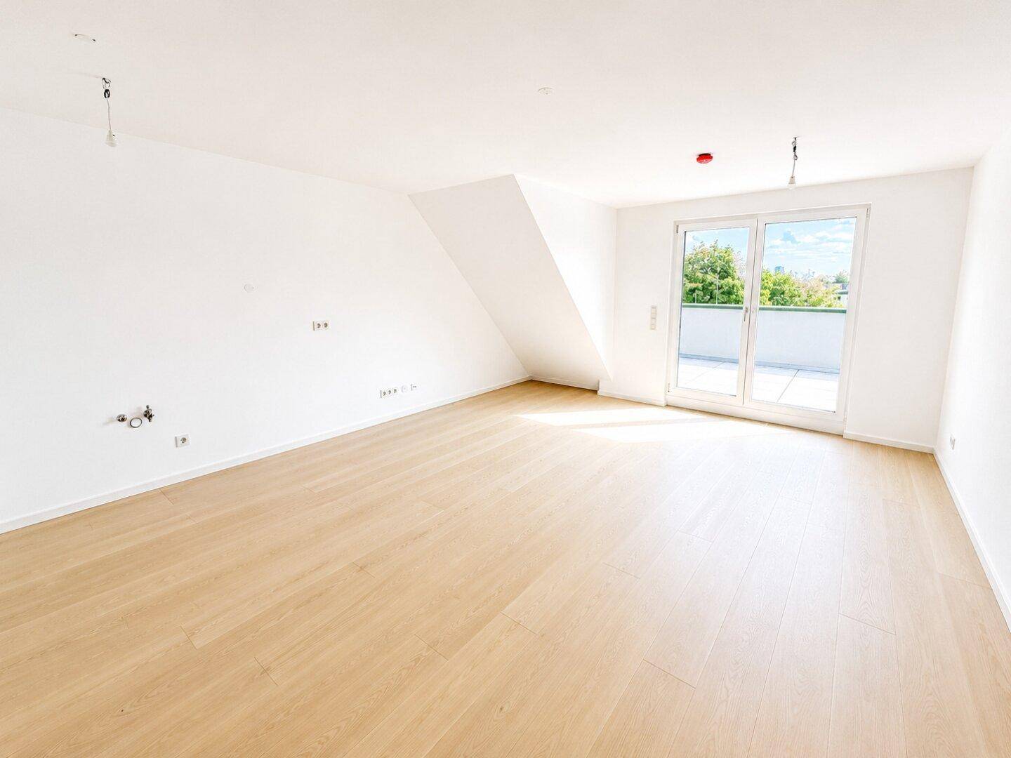 Heller, leerer Raum mit Holzboden, Dachschräge und Zugang zu einer Außenterrasse.