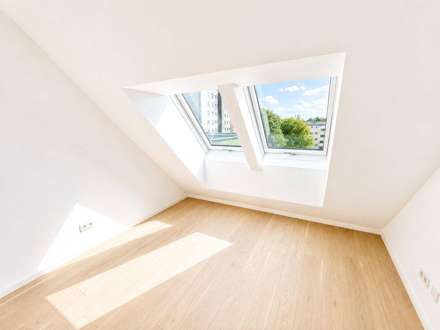 Lichtdurchfluteter Raum mit Holzboden, Dachschräge und großem Dachfenster mit Stadtblick.