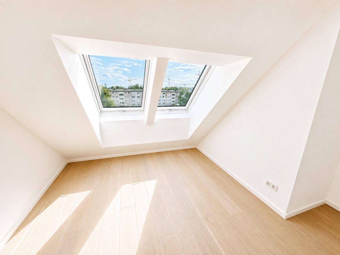 Heller Raum im Dachgeschoss mit Holzboden und zwei großen Dachfenstern für viel Tageslicht.