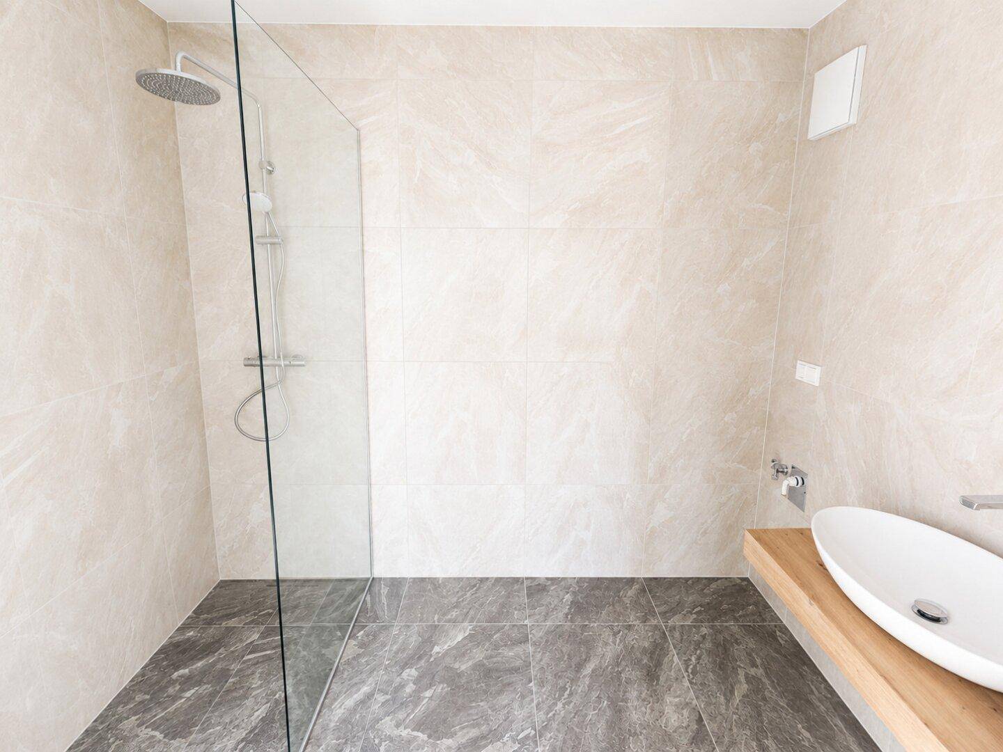 Modernes Badezimmer mit beigefarbenen Wandfliesen, begehbarer Dusche und elegantem Waschbecken.