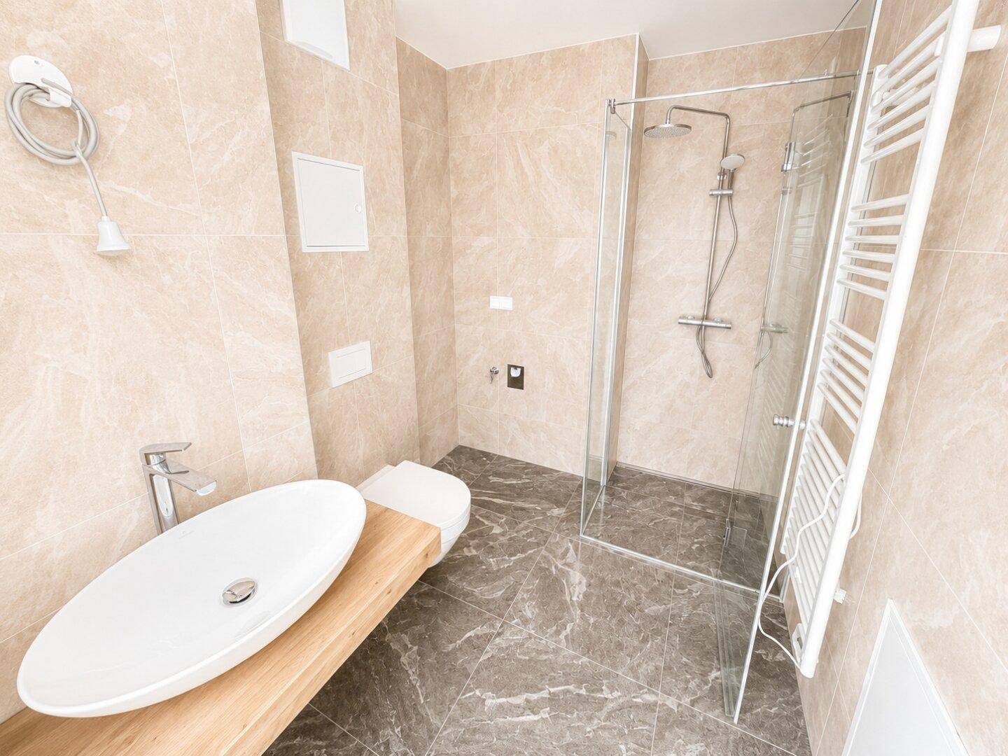 Modernes Badezimmer mit beigen Fliesen, ovalem Waschbecken und begehbarer Dusche.