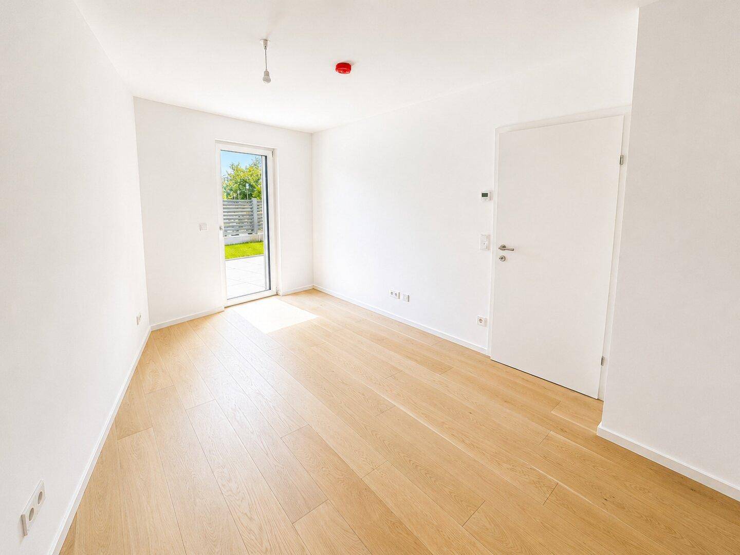 Helles, leeres Zimmer mit hellem Holzfußboden und Zugang zu einer Terrasse.